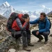 Dos montañistas en un sendero de alta montaña; uno está sentado con malestar y el otro lo asiste