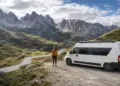 Camper blanca junto a una ruta de montaña con una persona mirando el paisaje
