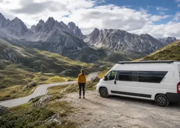 Camper blanca junto a una ruta de montaña con una persona mirando el paisaje