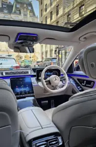 Rear view of a Mercedes-Benz interior with white seats, dashboard screen and city traffic ahead