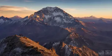 Dos montañistas frente a un gran macizo nevado de los Andes argentinos al amanecer